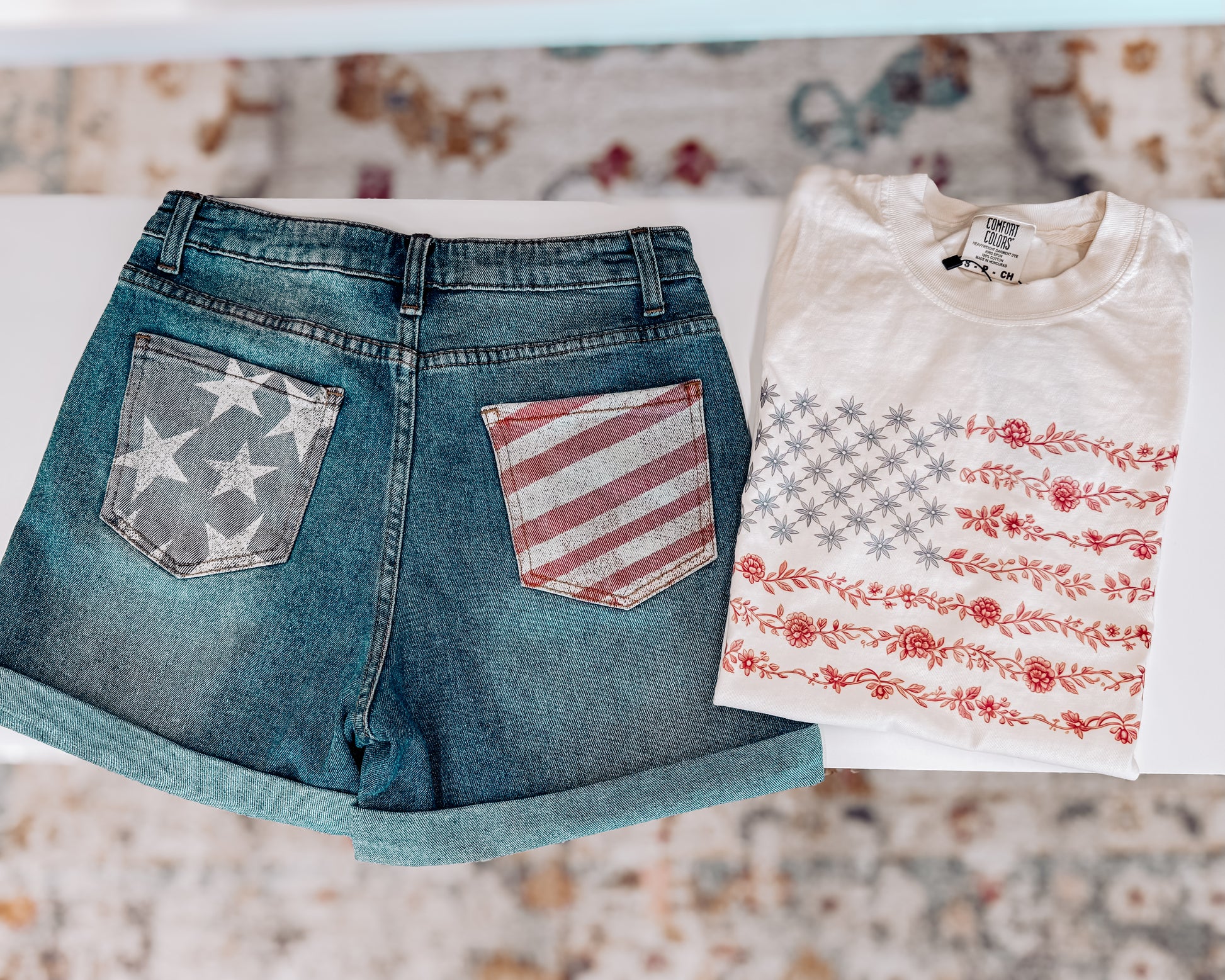 Cream-colored unisex t-shirt featuring a subtle and stylish American flag design made entirely of florals. The star field is composed of blue star-shaped flowers, while the red stripes are formed from intricate red floral garlands. This soft, vintage-inspired tee blends patriotic pride with a feminine, boho twist—perfect for summer celebrations like the Fourth of July, concerts, or casual weekends.