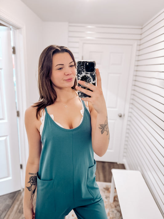 Dusty blue relaxed-fit jumpsuit with adjustable spaghetti straps and a scoop neckline. Features a slouchy, drop-crotch silhouette with deep side pockets and cuffed hems for a laid-back, comfy vibe. Made with ultra-soft stretch knit fabric, it’s perfect for lounging, errands, or layering over a tank or bralette for easy, everyday style.