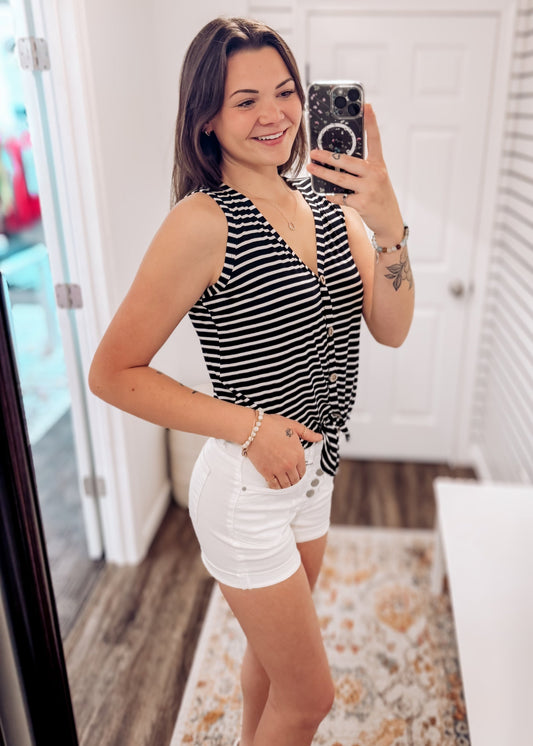 Woman wearing a sleeveless black and white horizontal striped tank top with a deep V-neckline and functional wooden buttons down the front. The top features a trendy front tie detail at the hem, creating a casual, flattering silhouette. Made from a soft, lightweight fabric, it's styled with medium-wash denim jeans—perfect for laid-back summer days, weekend outings, or everyday wear.