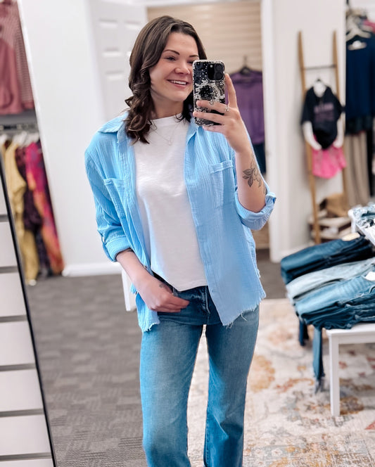 Lightweight and breezy button-down shirt in a soft, crinkled gauze fabric, featured in a fresh Spring Blue. Designed with dual chest pockets, raw-edge hem, and rolled long sleeves with button tabs. Slightly oversized fit for easy layering over tanks, tees, or swimsuits—perfect for casual days, lake life, or cool summer nights.
