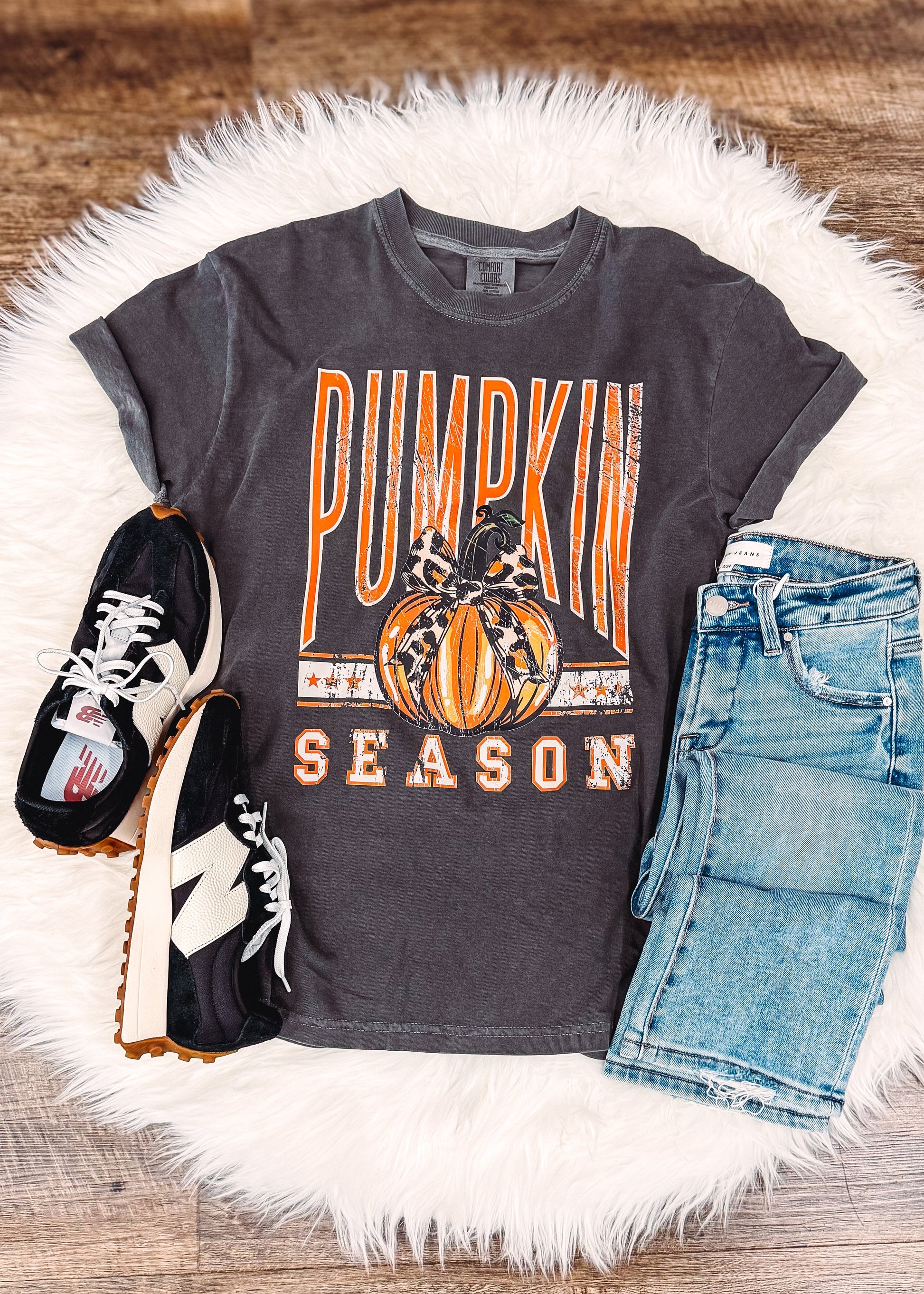 Gray t-shirt with 'Pumpkin Season' design, denim shorts, and black sneakers on a wooden surface.