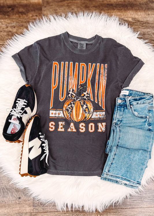 Gray t-shirt with 'Pumpkin Season' design, denim shorts, and black sneakers on a wooden surface.