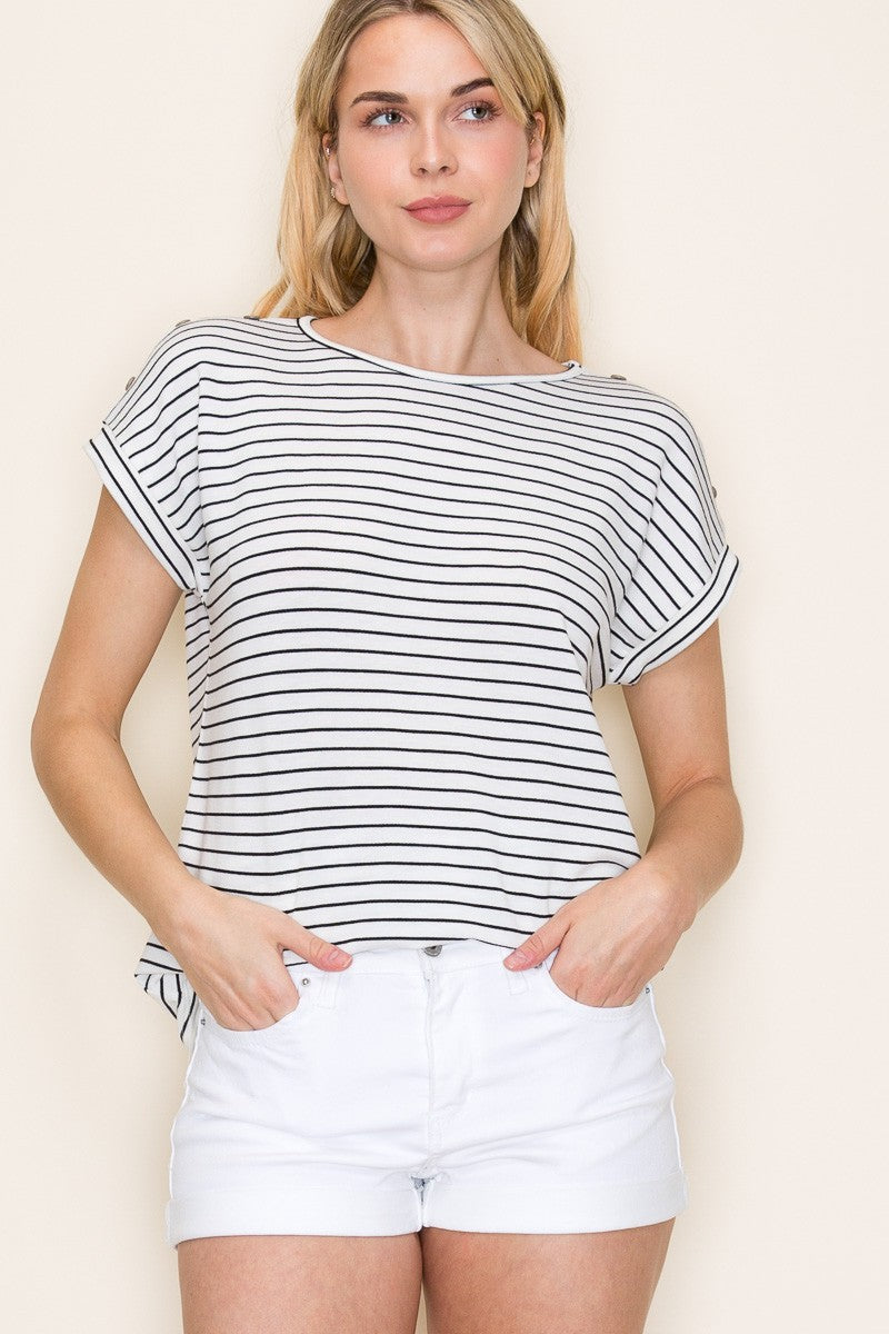 Woman wearing a white short-sleeve top with thin black horizontal stripes and rolled cuffs. The shirt features a relaxed, flowy fit with a crew neckline and button detail on the sleeves. Styled with white cuffed shorts, this effortless everyday tee is perfect for warm weather, offering a classic nautical-inspired look that’s both casual and polished.