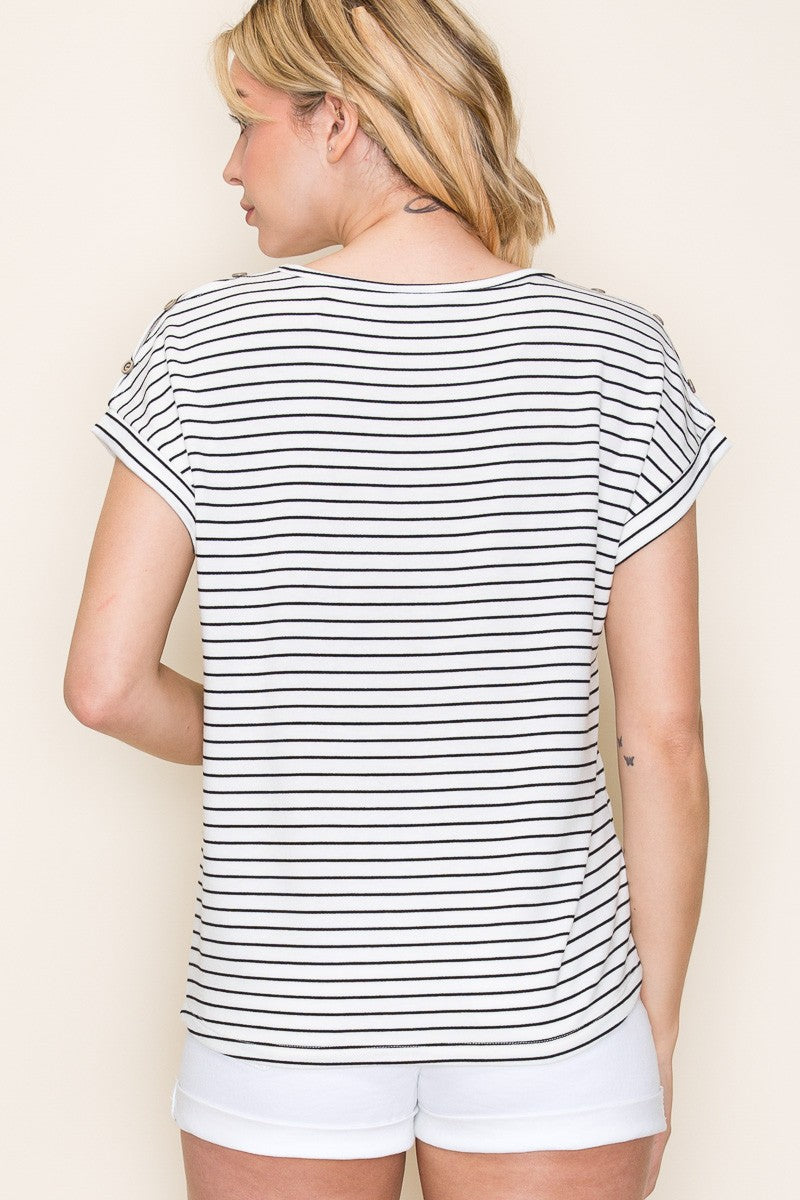 Woman wearing a white short-sleeve top with thin black horizontal stripes and rolled cuffs. The shirt features a relaxed, flowy fit with a crew neckline and button detail on the sleeves. Styled with white cuffed shorts, this effortless everyday tee is perfect for warm weather, offering a classic nautical-inspired look that’s both casual and polished.