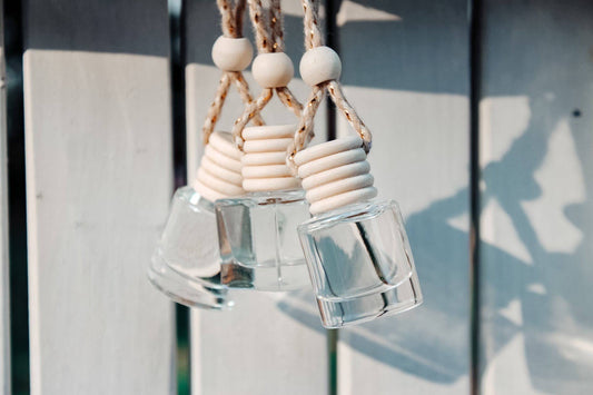 Three small clear glass shot glasses with stacked white ceramic lids and natural twine hanging loops, shown against a white wooden fence background with soft shadows.