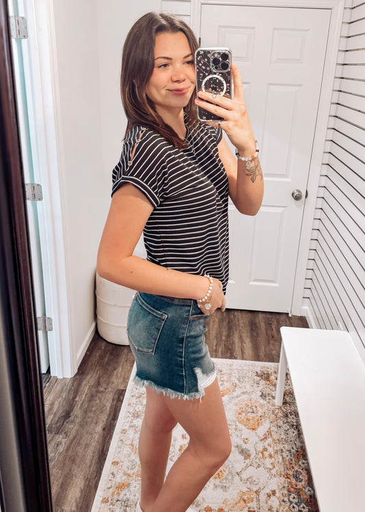 Woman wearing a black short-sleeve top with thin white horizontal stripes, a classic crew neckline, and rolled cuff sleeves with button accents. The top features a relaxed, drapey fit that pairs effortlessly with white cuffed shorts for a crisp, casual look. Perfect for everyday wear, this lightweight striped tee brings timeless style and comfort to your summer wardrobe.