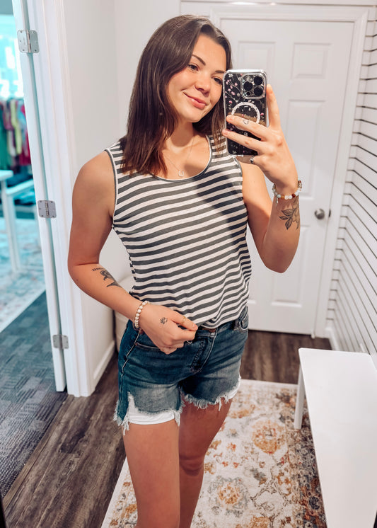 Woman wearing a casual sleeveless tank top with horizontal forest green and white stripes. The top features a scoop neckline and a relaxed, slightly flared silhouette that offers a breezy, comfortable fit. Styled with distressed dark-wash denim shorts, this easygoing look is perfect for everyday wear, beach days, or layering under summer cardigans and jackets.