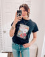 Black graphic tee featuring a bold vintage tattoo-inspired design with playing cards, flames, dice, pool balls, checkerboard accents, and red lips. Banner at the top reads “Life is a gamble, I’m just dealing.” Perfect for adding a little edge and attitude to your casual wardrobe—ideal for concerts, game nights, or days when you’re feeling a little wild.