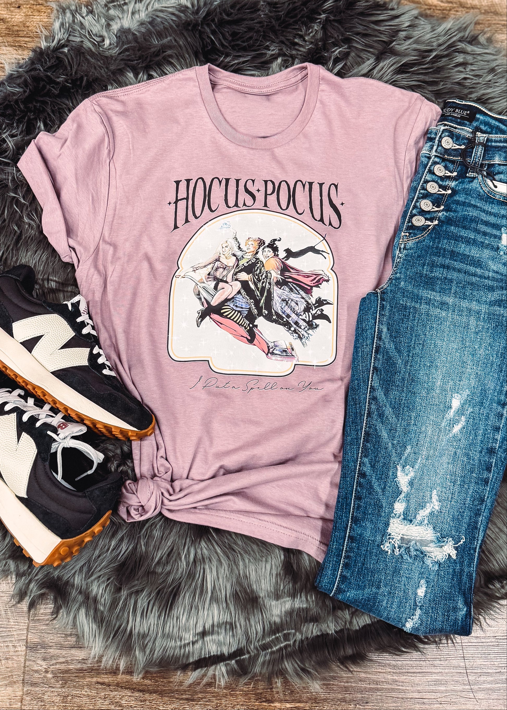 Pink t-shirt with graphic design, blue jeans, and sneakers on a fur rug.