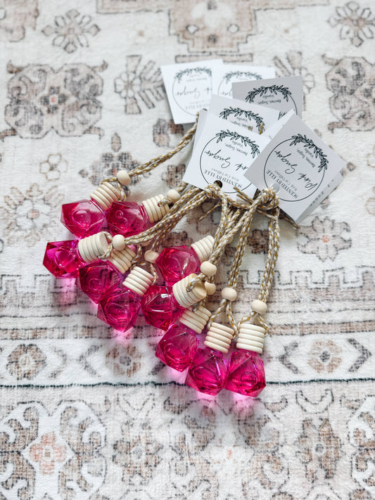 Four pink faceted crystal rose-shaped car fragrance diffusers tied with twine and attached to white paper tags, displayed on a patterned fabric background.