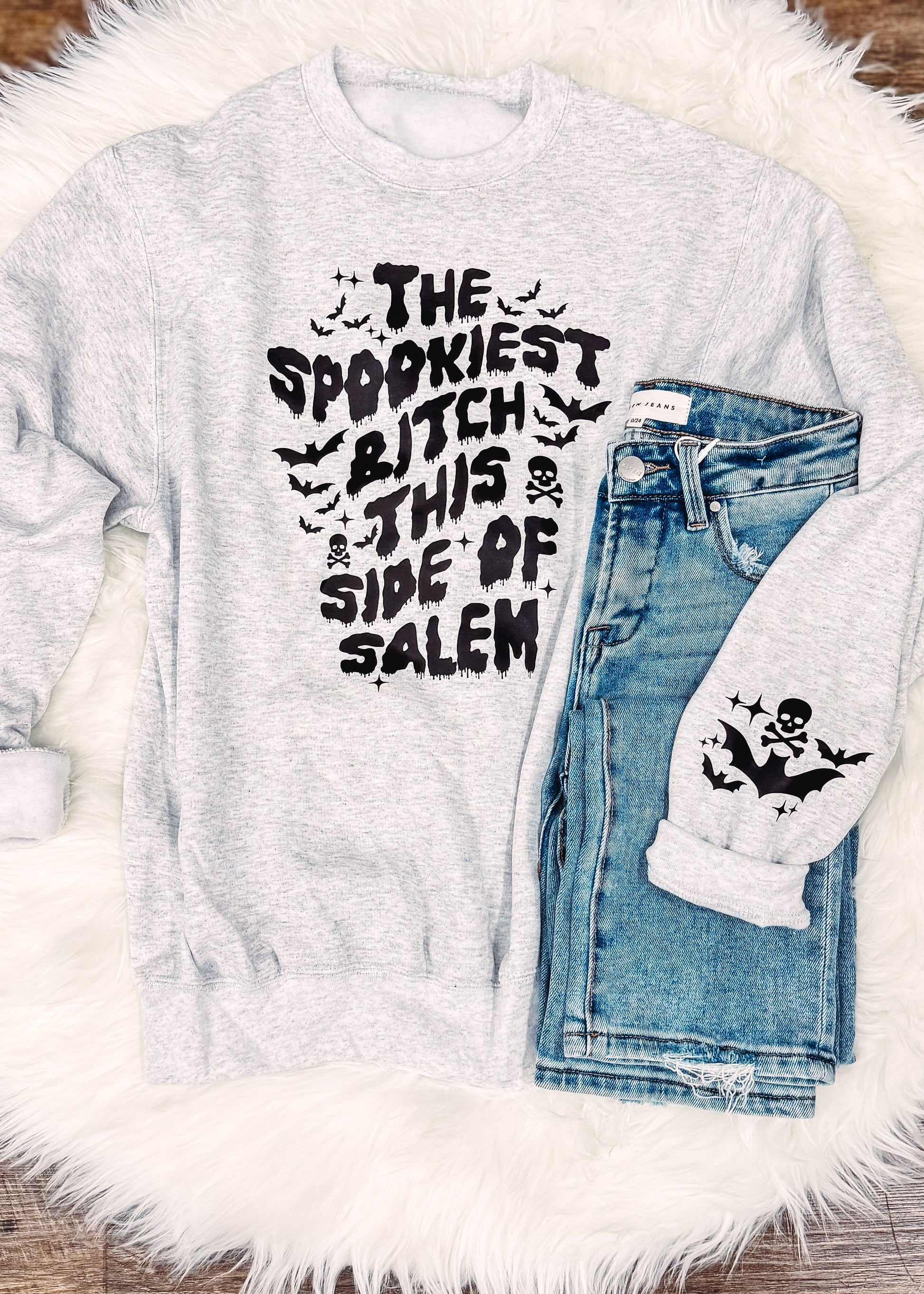 Gray sweatshirt with text and denim jacket on a fluffy white rug