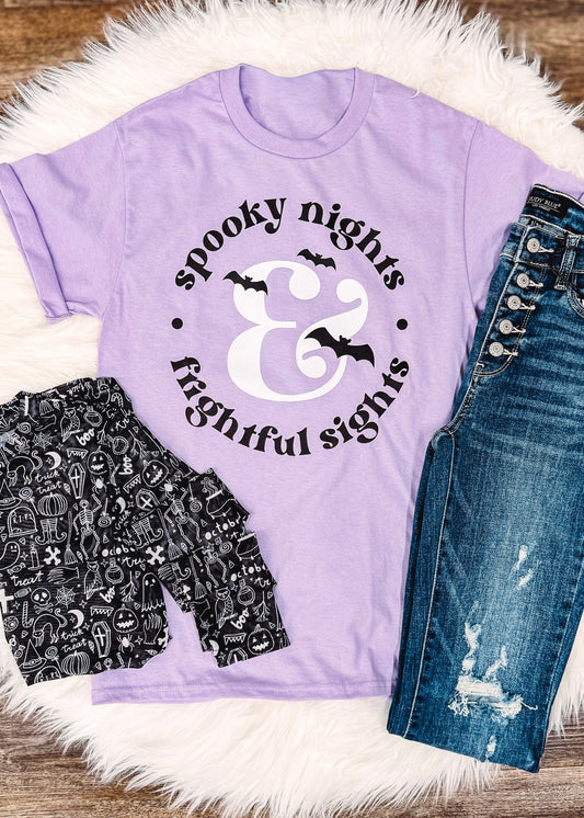 Purple t-shirt with Halloween design, black shorts, and blue jeans on a wooden surface.
