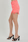 High-rise neon coral denim shorts with bold distressing and frayed hems. These eye-catching cutoffs feature a raw edge, angled hemline, and subtle peek-through front distressing for added flair. Designed with a crossover waistband and classic five-pocket construction. Perfect for adding a vibrant pop to your summer wardrobe—style with graphic tanks or breezy tees for a fun, playful look.