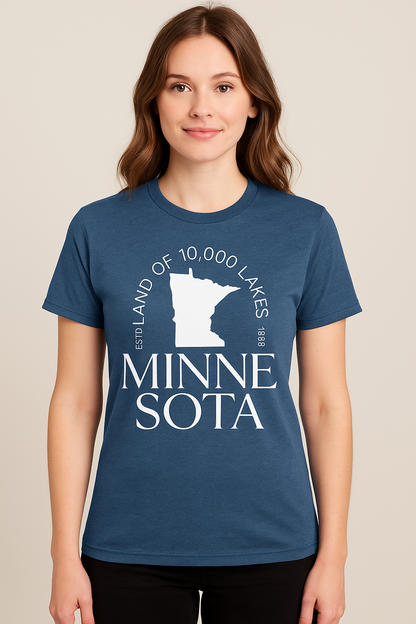 Heathered blue unisex t-shirt featuring a bold white graphic of the state of Minnesota, with the phrase “Land of 10,000 Lakes” encircling the silhouette. Below the graphic, elegant serif text reads “MINNESOTA” split across two lines. Includes subtle “ESTD 1858” details, nodding to the state's founding. Soft cotton-blend fabric with a classic fit—perfect for showing off Midwest pride in comfort and style.