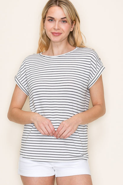 Woman wearing a white short-sleeve top with thin black horizontal stripes and rolled cuffs. The shirt features a relaxed, flowy fit with a crew neckline and button detail on the sleeves. Styled with white cuffed shorts, this effortless everyday tee is perfect for warm weather, offering a classic nautical-inspired look that’s both casual and polished.