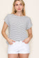 Woman wearing a white short-sleeve top with thin black horizontal stripes and rolled cuffs. The shirt features a relaxed, flowy fit with a crew neckline and button detail on the sleeves. Styled with white cuffed shorts, this effortless everyday tee is perfect for warm weather, offering a classic nautical-inspired look that’s both casual and polished.