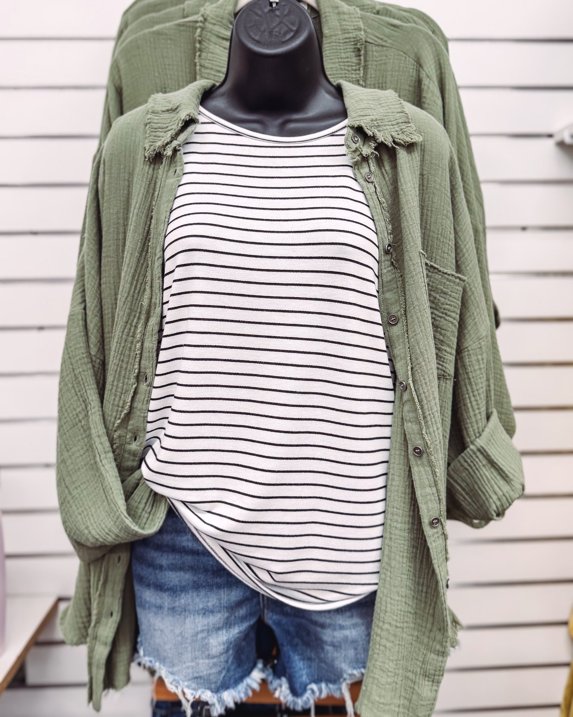 Women's oversized button-down shirt in light olive, crafted from a textured gauze fabric for a breathable and lived-in feel. Features raw-edge detailing on the collar and hem, front chest pocket, and functional button closures down the front. Drop shoulders and a relaxed fit make it ideal for layering over tanks or tees. A soft, casual essential for effortless cool-weather layering or breezy summer nights.