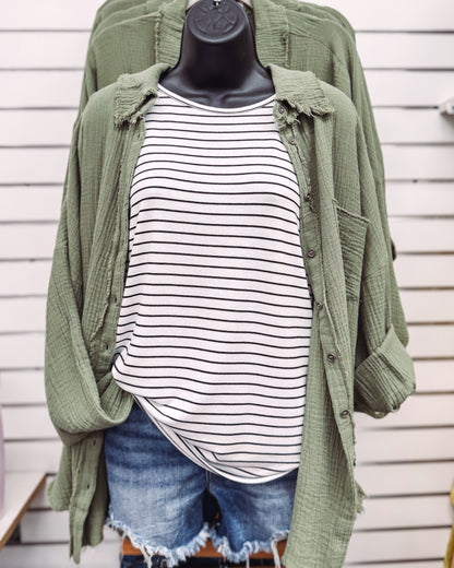 Women's oversized button-down shirt in light olive, crafted from a textured gauze fabric for a breathable and lived-in feel. Features raw-edge detailing on the collar and hem, front chest pocket, and functional button closures down the front. Drop shoulders and a relaxed fit make it ideal for layering over tanks or tees. A soft, casual essential for effortless cool-weather layering or breezy summer nights.