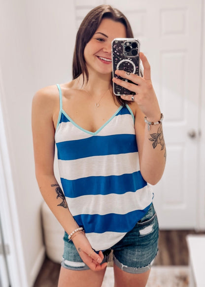 Woman wearing a blue and white striped tank top with a breezy, relaxed fit. The sleeveless top features bold horizontal stripes, a deep V-neckline, and contrasting aqua trim along the neckline and spaghetti straps. Lightweight and easygoing, this tank is paired with light-wash distressed denim shorts—perfect for summer days, beach trips, or casual outings with a fun pop of color.