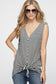 Woman wearing a sleeveless black and white horizontal striped tank top with a deep V-neckline and functional wooden buttons down the front. The top features a trendy front tie detail at the hem, creating a casual, flattering silhouette. Made from a soft, lightweight fabric, it's styled with medium-wash denim jeans—perfect for laid-back summer days, weekend outings, or everyday wear.