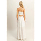 Woman wearing a white strapless smocked crop top and matching flowy tiered maxi skirt, standing against a neutral background.
