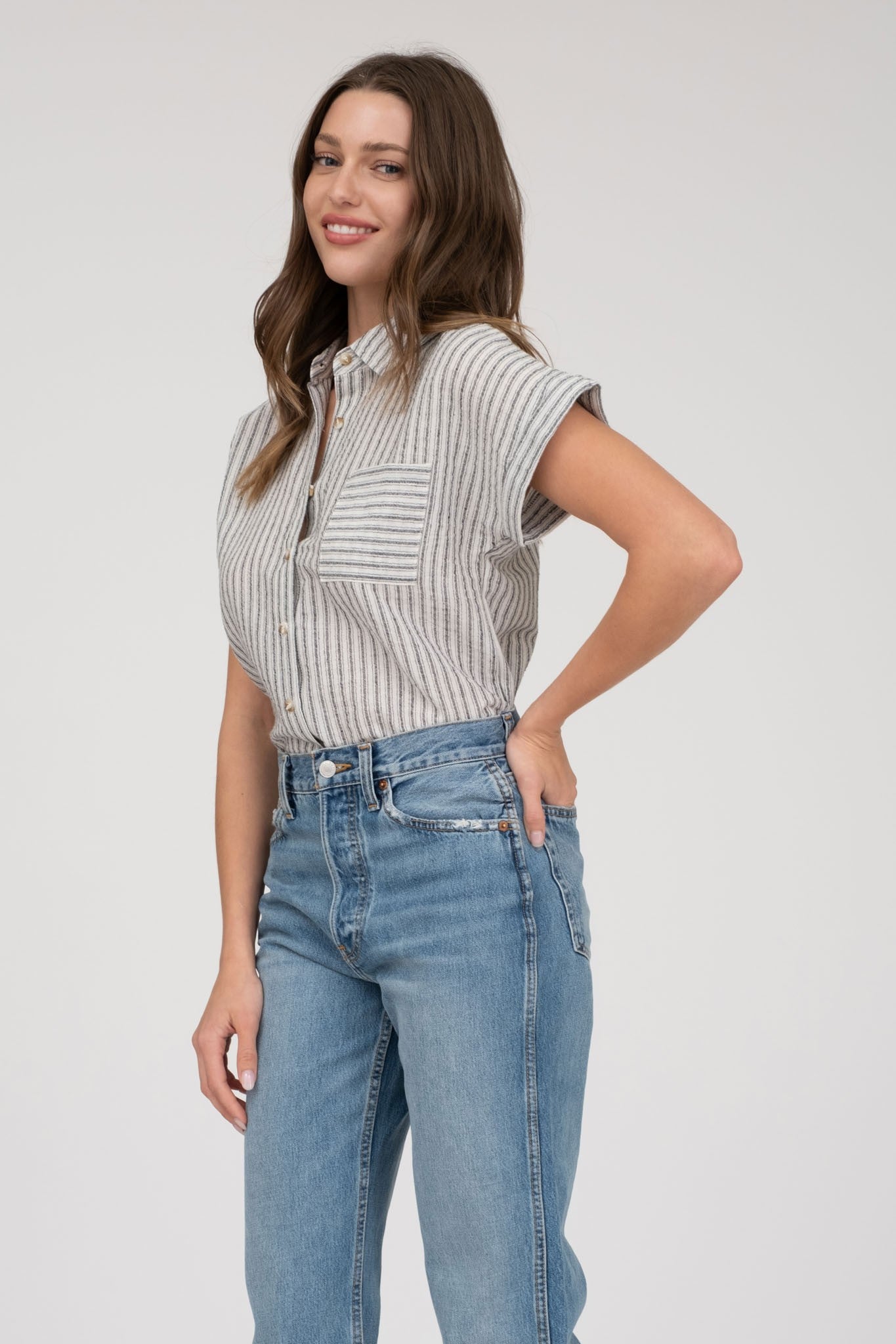 model wearing a short-sleeve button-up top with vertical black and white pinstripes. Features a collared neckline, front chest pocket with horizontal stripes for contrast, and a relaxed, slightly oversized fit. The shirt is styled with a black denim mini skirt, creating an effortlessly chic and casual look perfect for everyday wear