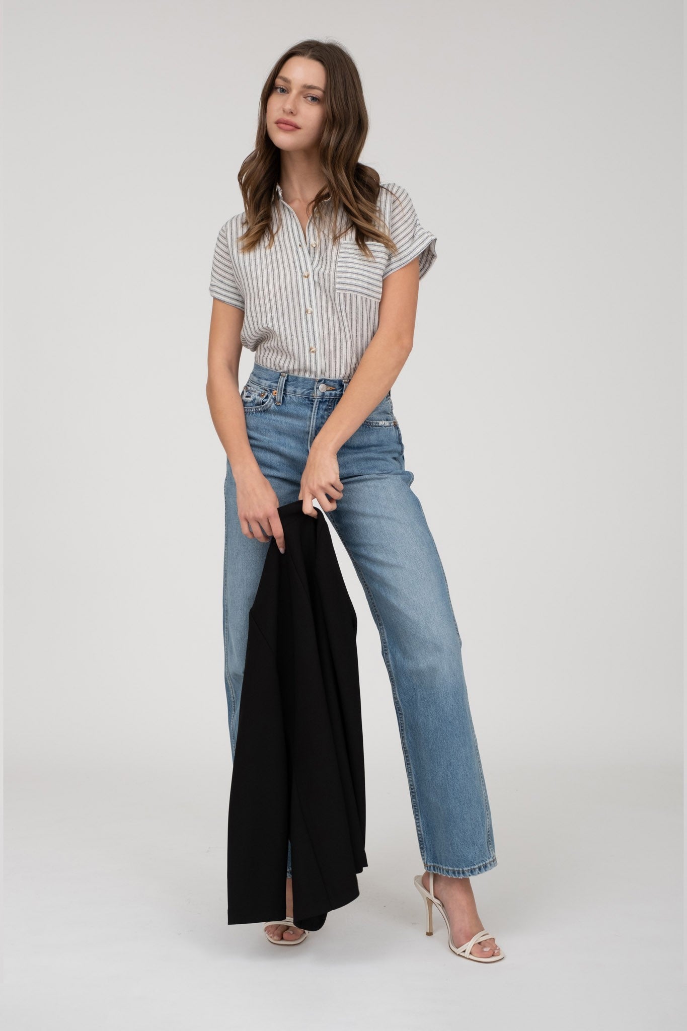 model wearing a short-sleeve button-up top with vertical black and white pinstripes. Features a collared neckline, front chest pocket with horizontal stripes for contrast, and a relaxed, slightly oversized fit. The shirt is styled with a black denim mini skirt, creating an effortlessly chic and casual look perfect for everyday wear