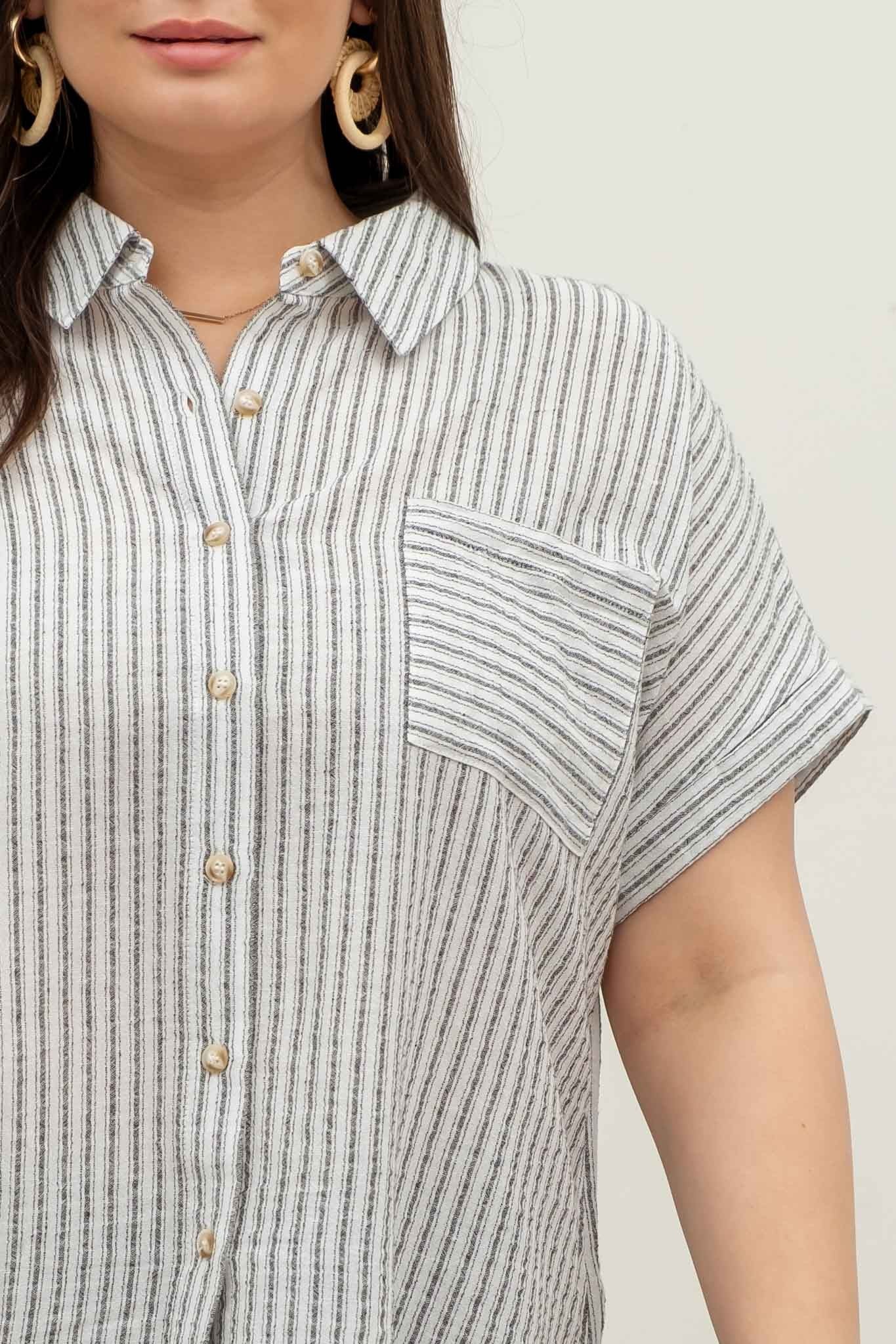 model wearing a short-sleeve button-up top with vertical black and white pinstripes. Features a collared neckline, front chest pocket with horizontal stripes for contrast, and a relaxed, slightly oversized fit. The shirt is styled with a black denim mini skirt, creating an effortlessly chic and casual look perfect for everyday wear