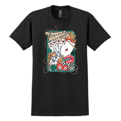 Black graphic tee featuring a bold vintage tattoo-inspired design with playing cards, flames, dice, pool balls, checkerboard accents, and red lips. Banner at the top reads “Life is a gamble, I’m just dealing.” Perfect for adding a little edge and attitude to your casual wardrobe—ideal for concerts, game nights, or days when you’re feeling a little wild.