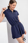 Navy short sleeve romper with a sporty polo-style collar and quarter zip neckline. Features an elastic waistband for a flattering fit and a flowy skirted bottom that offers both movement and comfort. Made from recycled polyester for an eco-conscious touch. A versatile one-piece perfect for active days, travel, or casual outings.