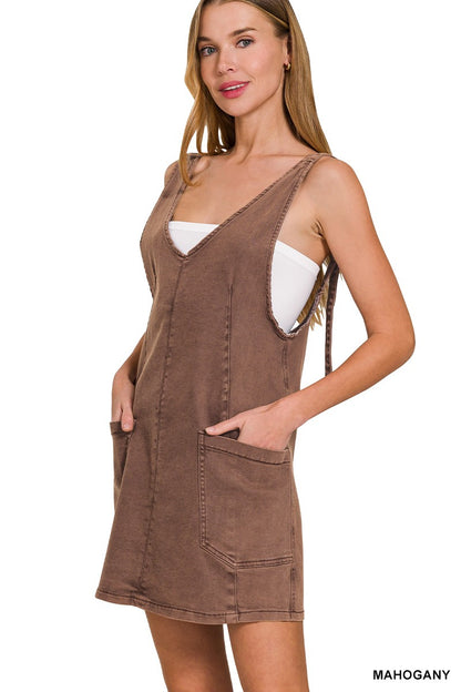 Sleeveless mahogany overall-style dress with a soft, washed finish and relaxed silhouette. Features a deep V-neckline, wide shoulder straps with tie-back detail, and oversized front patch pockets. Slightly A-line cut with above-the-knee hem for easy, breezy styling. Perfect for layering over tanks or bralettes for a casual, warm-weather look.